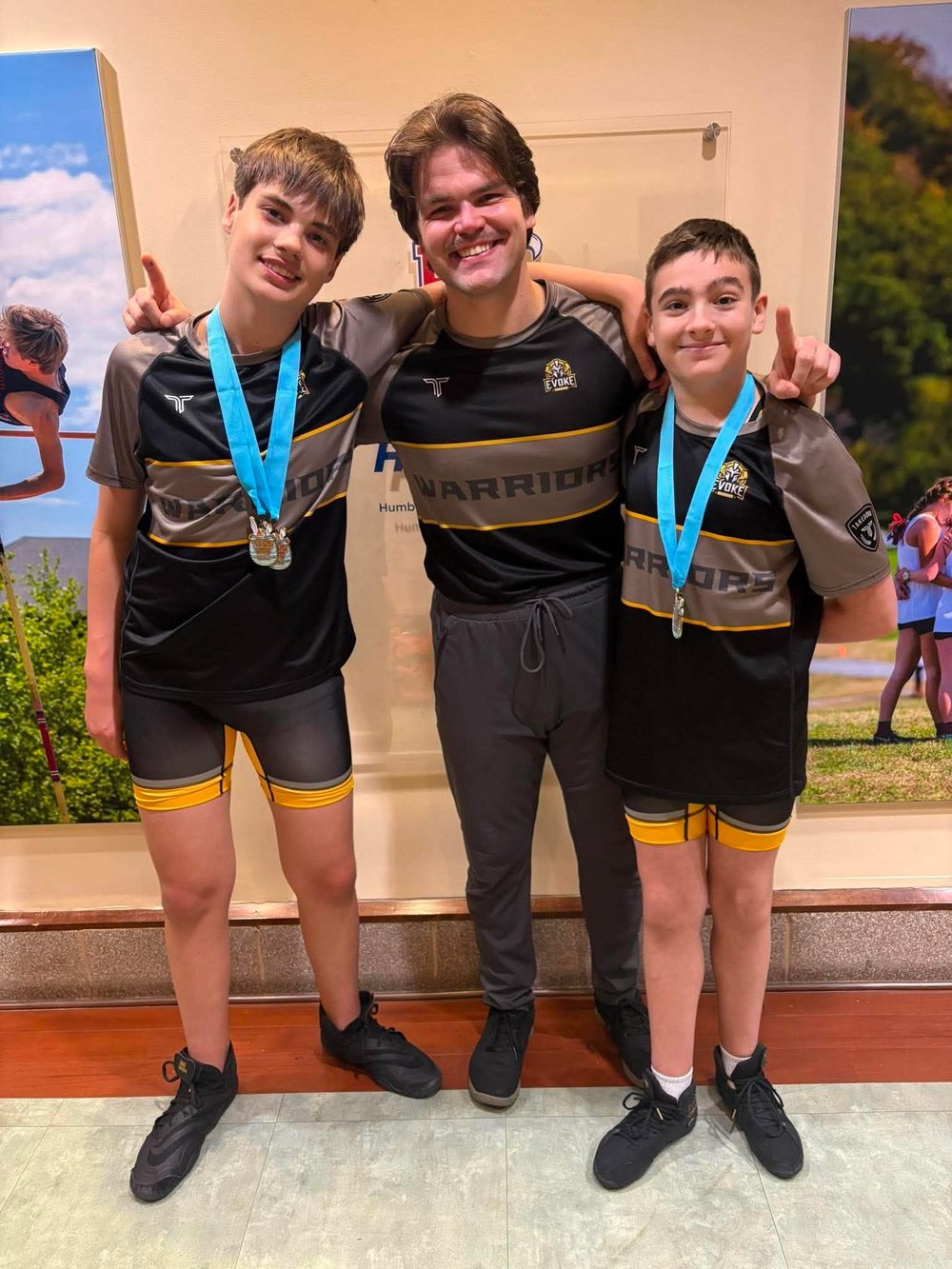 Coach Devin with two Warriors wrestlers wearing their tournament medals